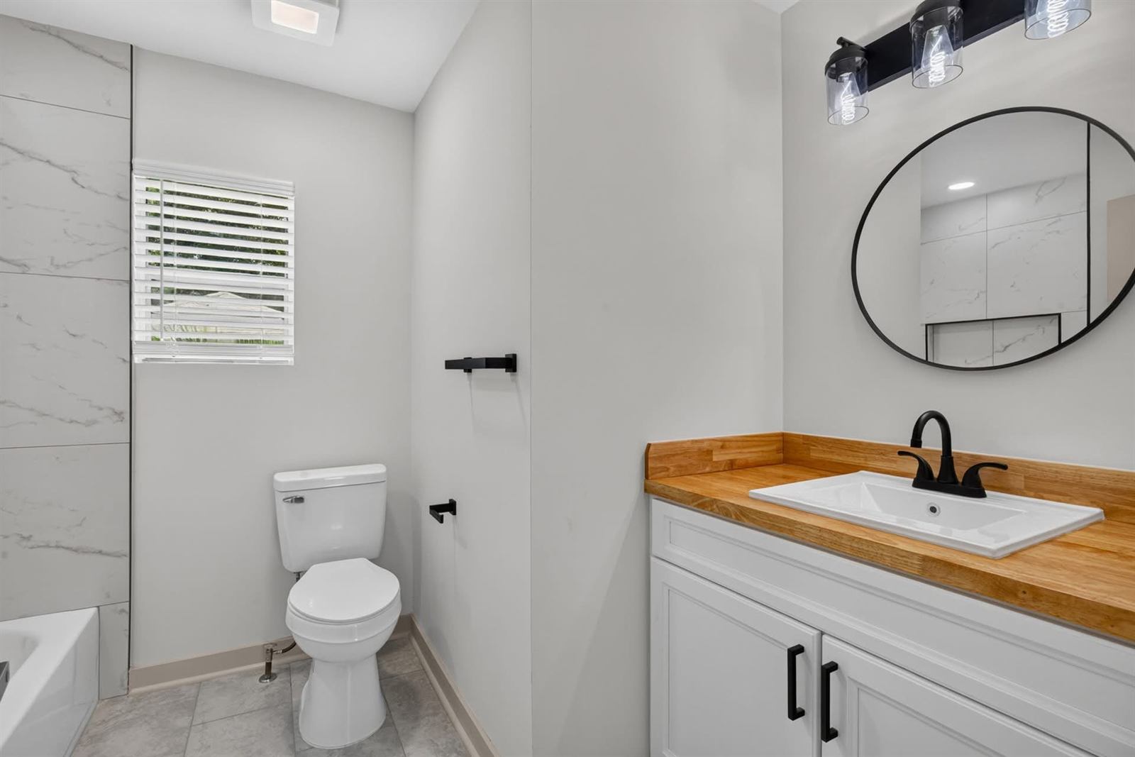The same bathroom after renovation with large-format tile, new vanity with butcher block top and matte black fixtures