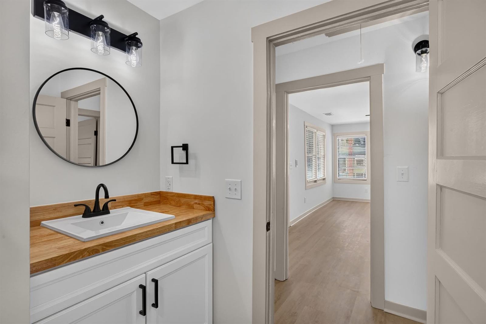 Renovated bathroom vanity with butcher block top, round mirror and matte black fixtures