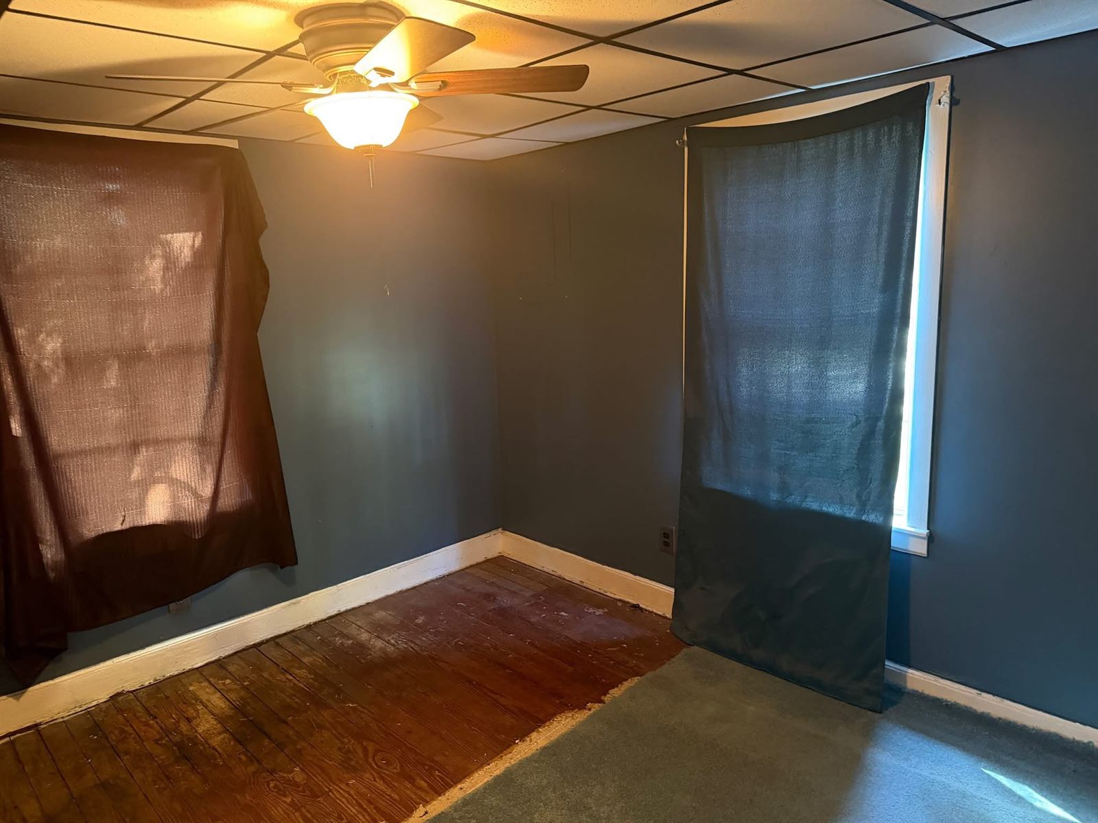 Bedroom before renovation with dark walls, exposed subfloor and partial carpet