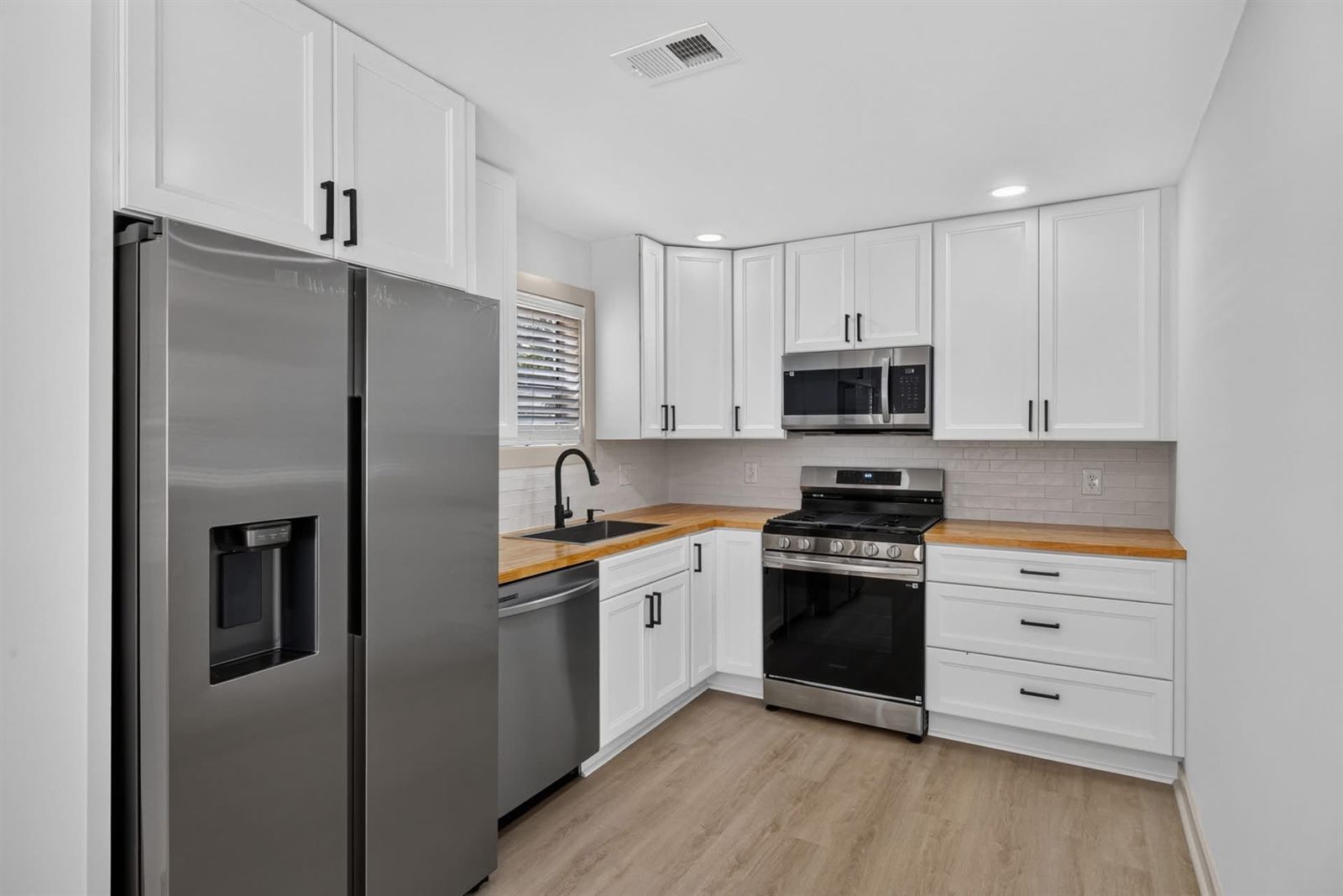 Renovated fix and flip kitchen with white cabinets, butcher block counters and stainless appliances